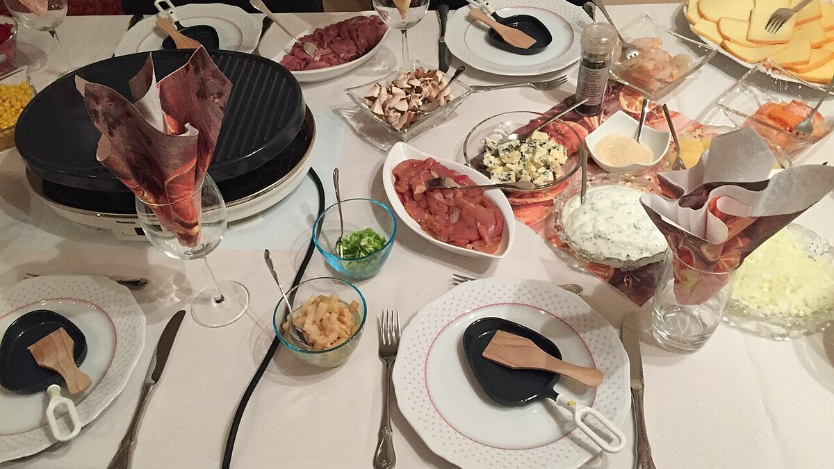 Table de raclette avec appareil, fromage, pommes de terre et accompagnements